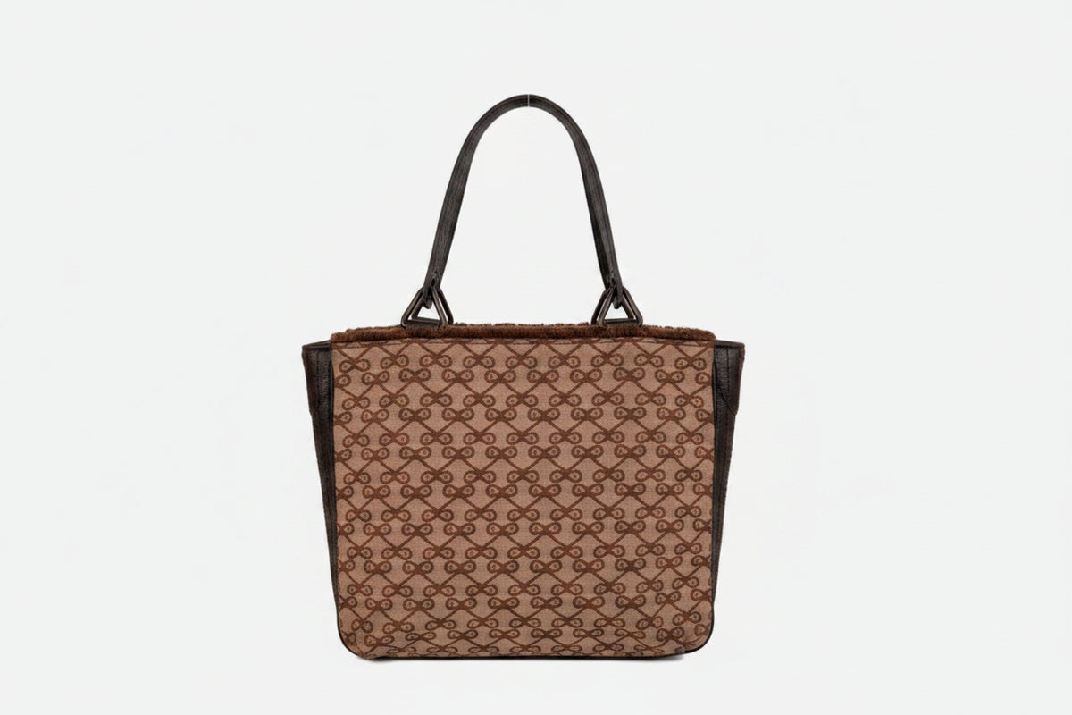 Brown patterned handbag on a gold stand against a white background